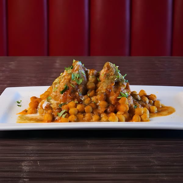 Pakwan Indian restaurant's samosa chaat, topped with chickpeas, sauces, and fresh cilantro on a white plate.
