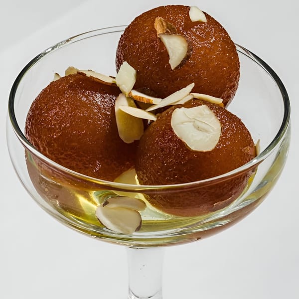 Three gulab jamun, garnished with almond slivers, soaking in syrup within a clear glass bowl.