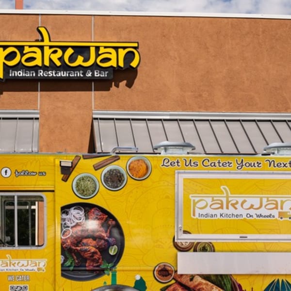 Pakwan Indian Restaurant & Bar sign above a yellow food truck with Indian food graphics.