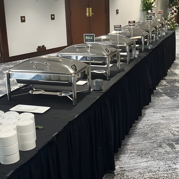 A long buffet table with several silver chafing dishes and stacks of white plates.