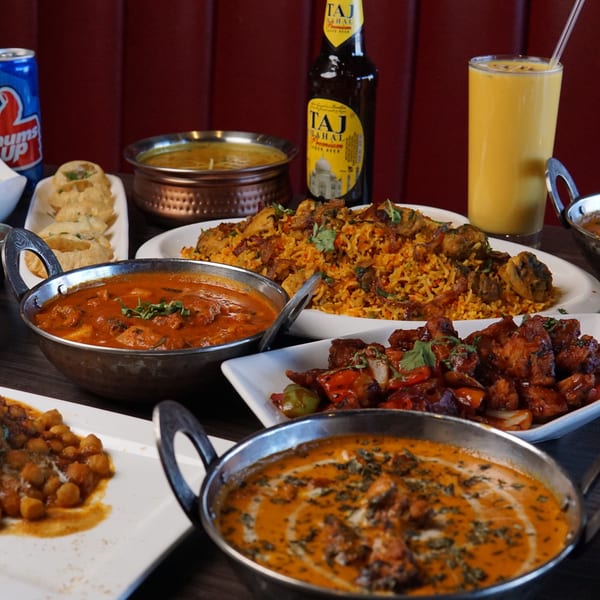 A table laden with various Indian dishes, including curries, biryani, appetizers, and drinks.