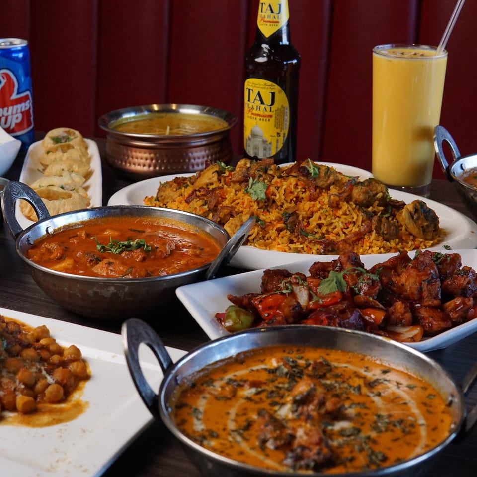 A table laden with various Indian dishes, including curries, biryani, appetizers, and drinks.