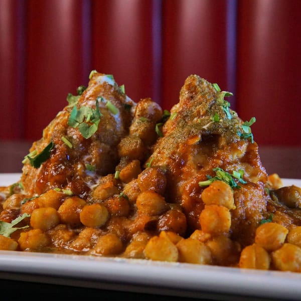 Two samosas topped with sauce and cilantro, surrounded by chickpeas on a white plate.