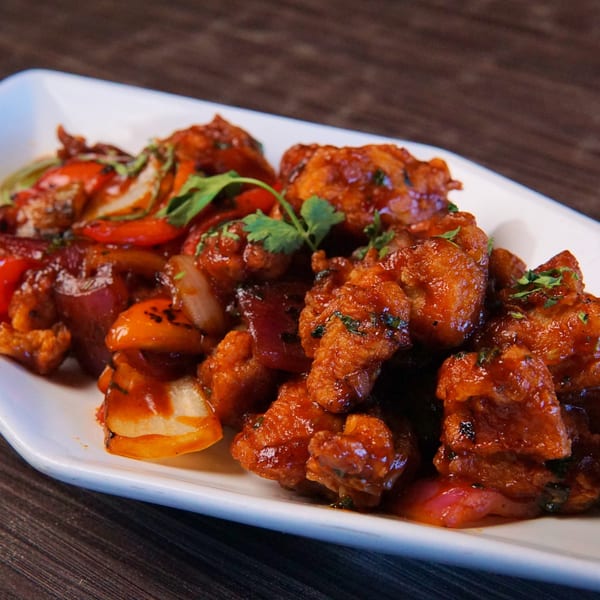 Close-up of chili chicken with bell peppers and onions, garnished with cilantro on a white plate.